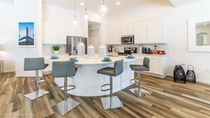 A modern kitchen with white cabinets, a central island with bar stools, stainless steel appliances, and pendant lighting. - Solterra Exec Villas- 6136bod (Davenport)