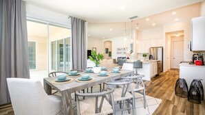 A modern kitchen with white cabinets, a stainless steel refrigerator, and a dining area with a wooden table and chairs. - Solterra Exec Villas- 6136bod (Davenport)