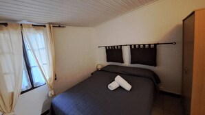 Una cama individual con un edredón oscuro, una mesita de noche con una lámpara y una ventana con cortinas.