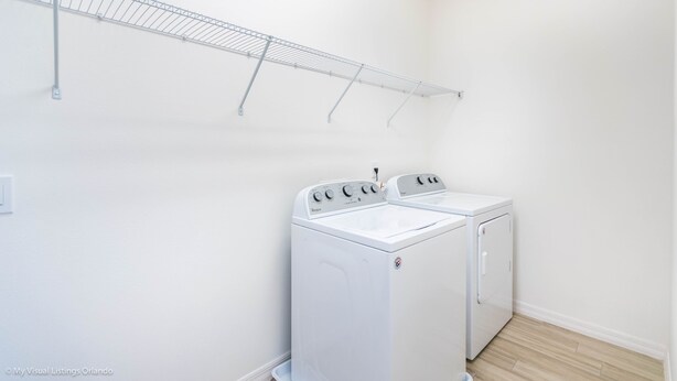 A laundry room with two white washing machines, a metal drying rack, and a wooden floor. - Solterra Exec Villas- 6112bod (Davenport)