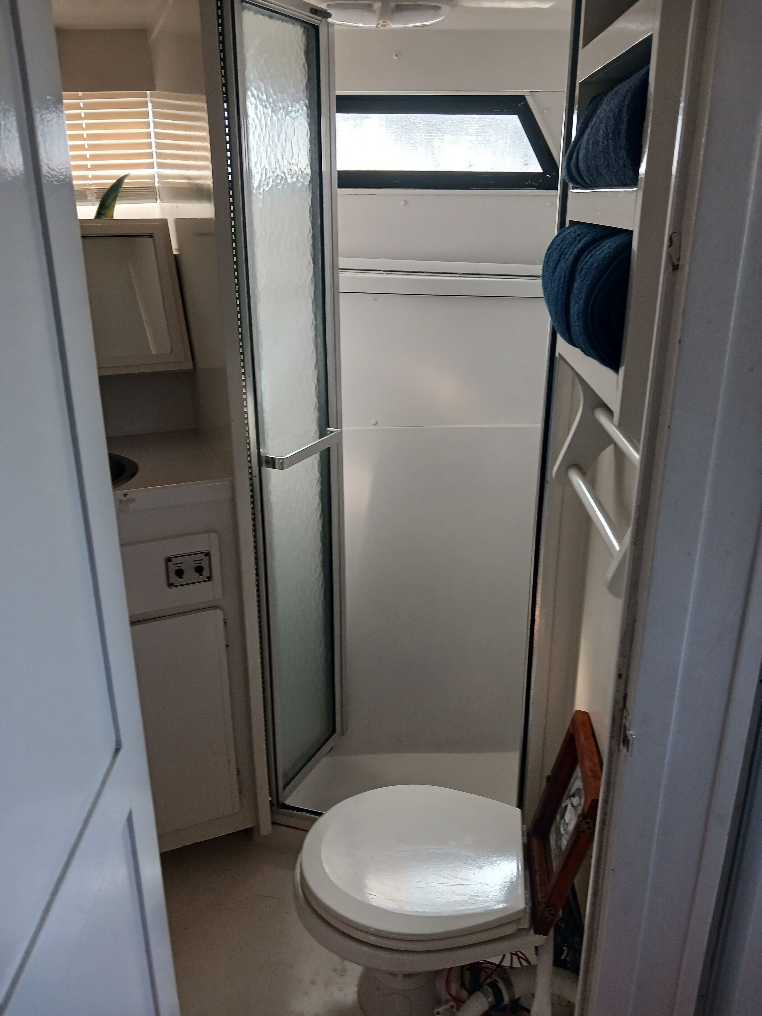 A compact bathroom with a toilet, a small sink, and a window with blinds.