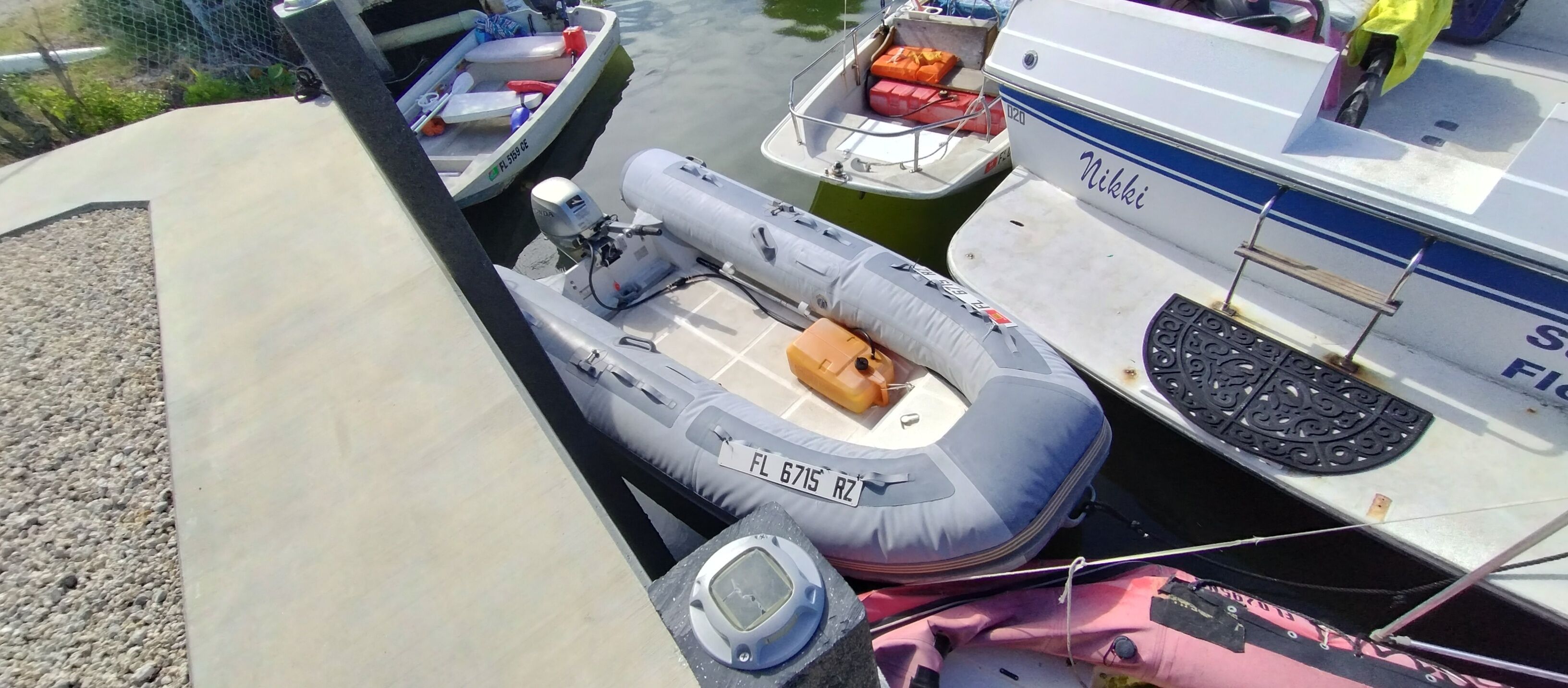 A row of boats docked at a marina, including a motorized inflatable boat and a motorboat with a cabin.