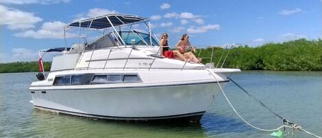 A white boat with two people on deck, a canopy, and a clear sky.