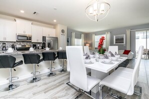 A modern kitchen with white cabinets, stainless steel appliances, and a dining area with white chairs and a white table set for six.