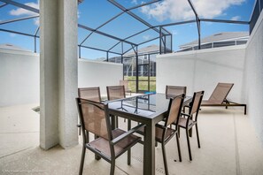 A covered outdoor dining area with a glass table and chairs, surrounded by white walls and concrete pillars.