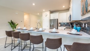 A modern kitchen with a central island, bar stools, and a clock on the wall. - Champions Gate Exec Villas- 1670mvd (Davenport)