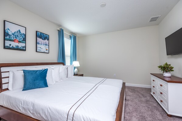 A bedroom with a large bed, a nightstand with a lamp, a dresser, and two framed pictures on the wall.