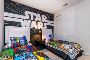 A Star Wars-themed bedroom with two beds, a wall mural, and a nightstand.