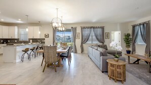 A spacious living area with a dining table, sofa, and a kitchen in the background. - Champions Gate Exec Villas- 8908sd (Davenport)
