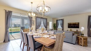 A dining area with a wooden table, chairs, and a chandelier. There is a sofa and a television in the background. - Champions Gate Exec Villas- 8908sd (Davenport)