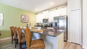 A kitchen with white cabinets, a stainless steel refrigerator, a microwave, and a clock on the wall. - Champions Gate Exec Villas- 9053dld (Davenport)