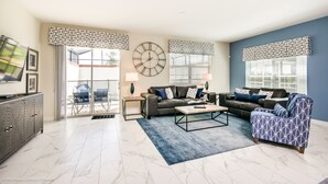 A spacious living room with a sofa, armchair, and coffee table. There is a clock on the wall and a TV on the left. - Champions Gate Exec Villas- 8917stinger (Davenport)