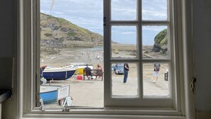 A view through a window of a coastal area with boats, a beach, and cliffs. - Harbour Loft - Two Bedroom Apartment, Sleeps 4 (Port Isaac)