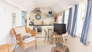 A cozy kitchen with wicker furniture, a television, and a clock on the wall. - Harbour Loft - Two Bedroom Apartment, Sleeps 4 (Port Isaac)
