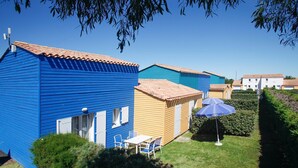 A row of colorful holiday cottages with tiled roofs, a small table with chairs, and a blue umbrella.