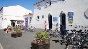 A building with a white facade, a blue door, and a sign for Odalys Accueil. There are bicycles parked outside and flower planters in the foreground.