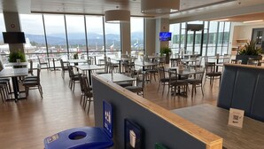 Un comedor moderno con varias mesas y sillas, una estación de reciclaje y vistas a montañas a través de amplios ventanales.