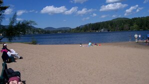 Una playa junto al lago con gente relajándose en la arena y sillas.