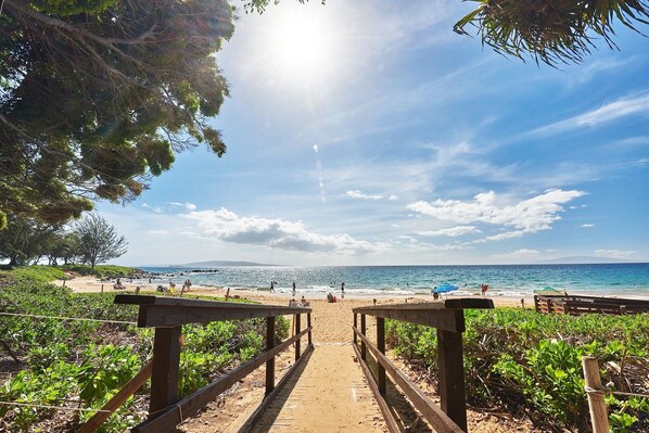 Un sendero de madera que lleva a una playa con cielos despejados y vista al océano.