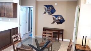 A dining area with a glass-top table, wooden chairs, a wooden sideboard, and two wall-mounted decorative fish.