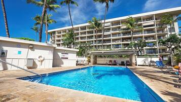 A hotel with a swimming pool, palm trees, and a multi-story building.