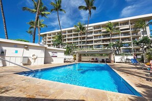 Um hotel com piscina, palmeiras e um edifício de vários andares.