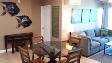 A living room with a glass-top dining table surrounded by chairs, a sofa, and a wall-mounted air conditioner.