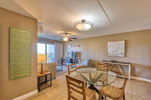 A spacious living room with a glass-top dining table, wooden chairs, a ceiling fan, a television, and a sofa.