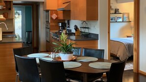A modern kitchen with wooden cabinets, a dining area with a table set for four, and a clock on the wall. - Hilltop Hideaway, cozy forest retreat, Portland (Portland)