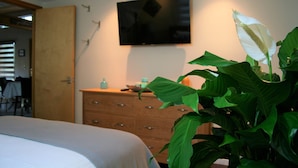 A bedroom with a bed, a dresser, a television mounted on the wall, and a large green plant. - Hilltop Hideaway, cozy forest retreat, Portland (Portland)