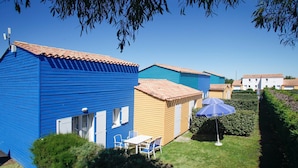 A row of colorful holiday cottages with tiled roofs, a small table with chairs, and a blue umbrella.