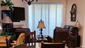 Un comedor con una mesa redonda, seis sillas, una araña y un ventilador de techo.