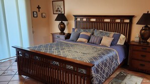 Un dormitorio con una cama de madera, dos mesitas de noche, un aparador de madera y dos lámparas de pared.