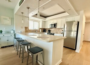 A modern kitchen with a central island, bar stools, stainless steel appliances, and a checkered backsplash.
