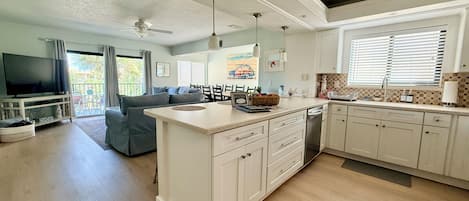 A modern kitchen with a central island, a dining area with a sofa, and a TV in the living room.
