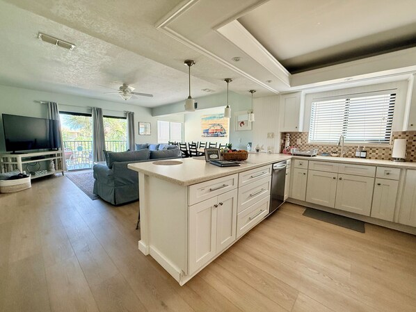 A modern kitchen with a central island, a dining area with a sofa, and a TV in the living room.