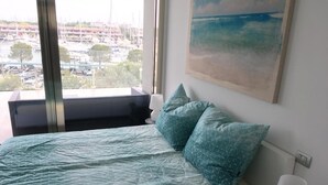A bedroom with a bed, two pillows, a nightstand, a lamp, and a painting of a beach.