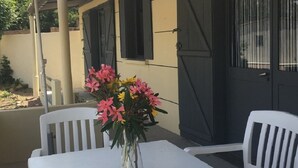 En patio med et bord og stole, en vase med blomster, og en bygning med vinduer og en dør i baggrunden.