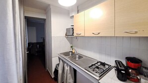 Et kompakt køkken med hvide skabe, en stålvask, gasblus og en brødrister.