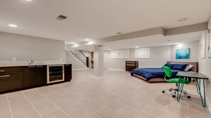 A spacious living area with a kitchen, a staircase, a bedroom with a bed and green chair, and a small table.