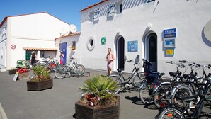 A building with a white facade, a blue door, and a sign for Odalys Accueil. There are bicycles parked outside and flower planters in the foreground. - Appart authentique et au calme, à 300m de la plage (Ile d'Oleron)