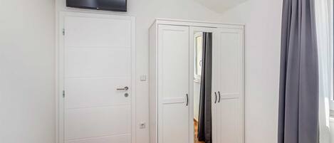 Een kamer met een witte kast, een wandtelevisie en een raam met grijze gordijnen.