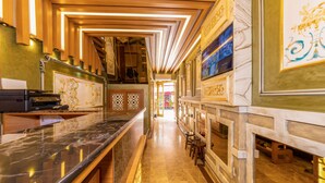 Un hall d’hôtel doté d’un comptoir de réception en marbre, de décorations murales élaborées et d’un escalier menant aux étages supérieurs.