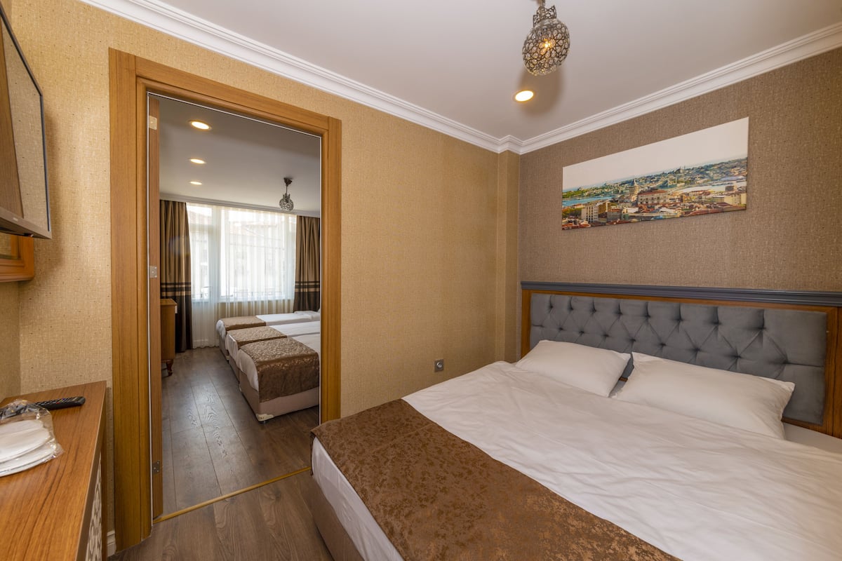 A hotel room with a large bed, a smaller bed, a wooden desk, a mirror, and a painting on the wall.