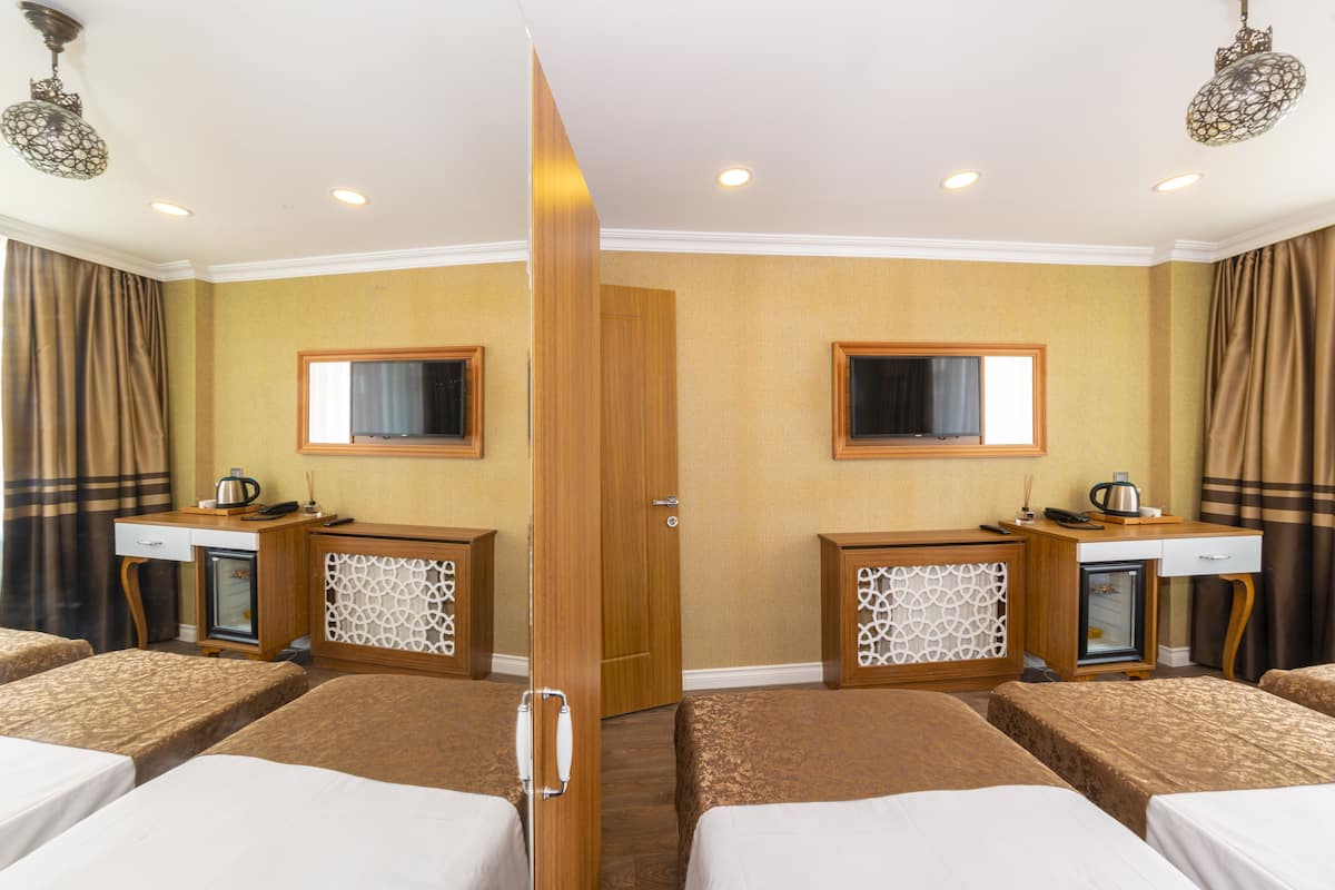 A hotel room with two beds, a wooden wardrobe, a desk with a mirror, and a small cabinet.