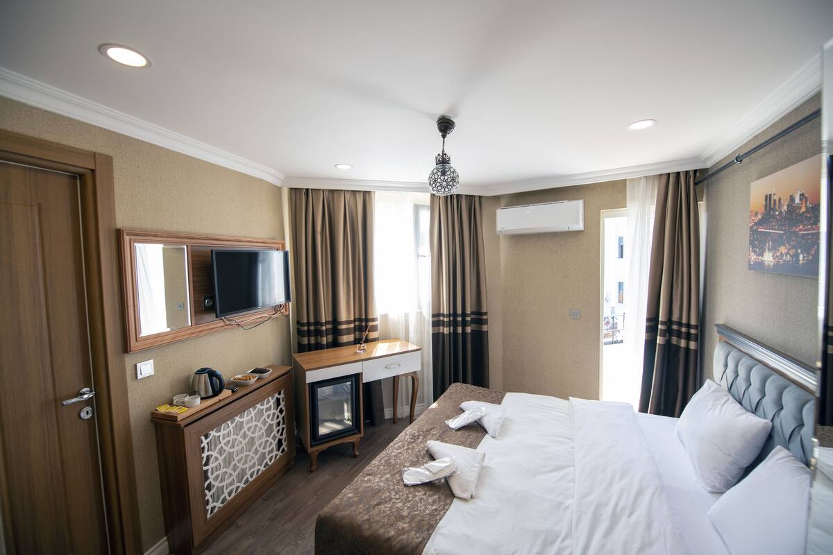 A hotel room with a bed, a desk, a television, and a window with curtains.