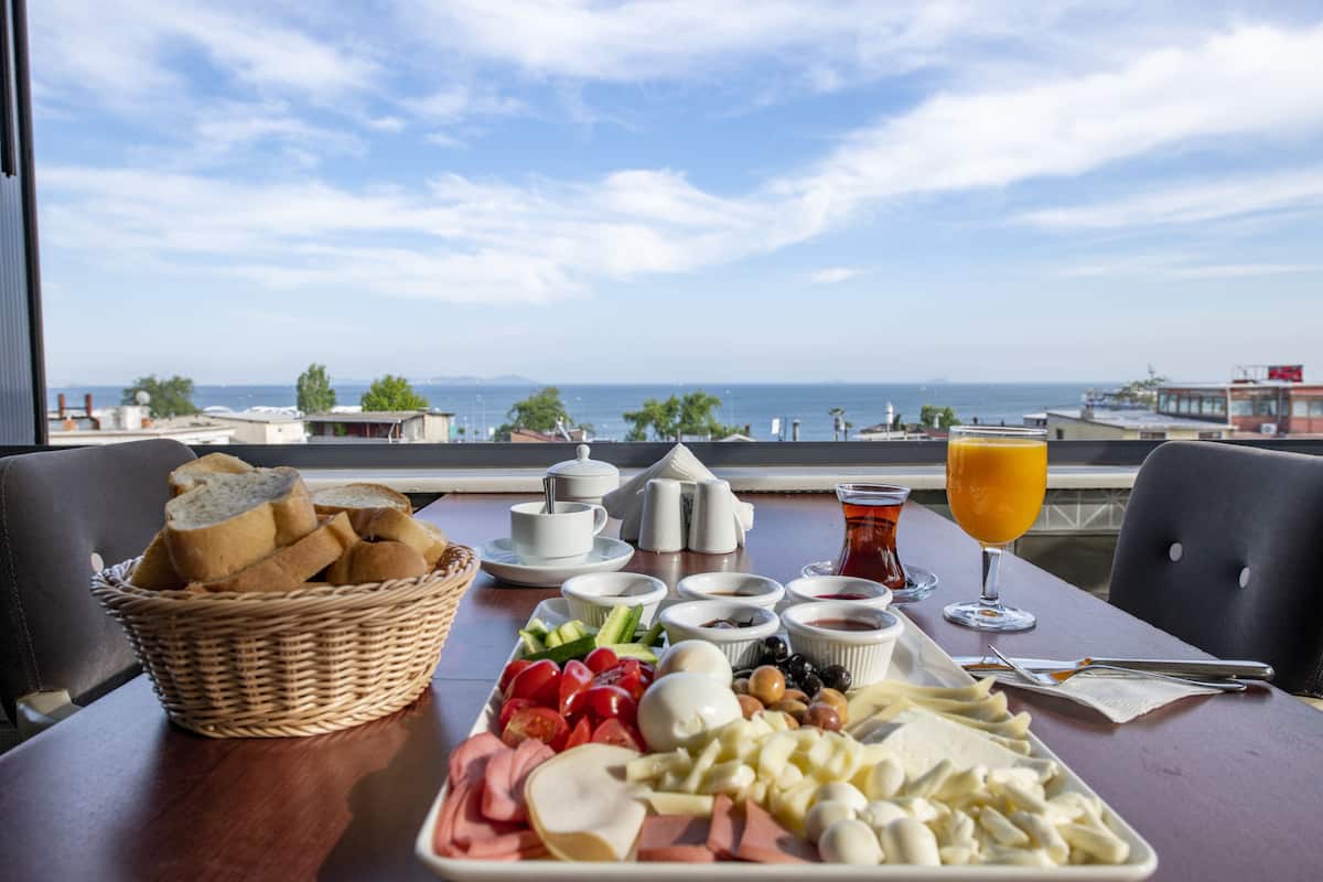 A breakfast table with a variety of foods and a glass of orange juice, overlooking a scenic view of the sea and buildings.