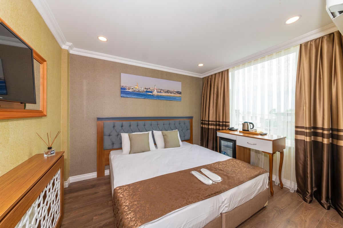A hotel room with a large bed, a desk, a television, and a window with curtains.