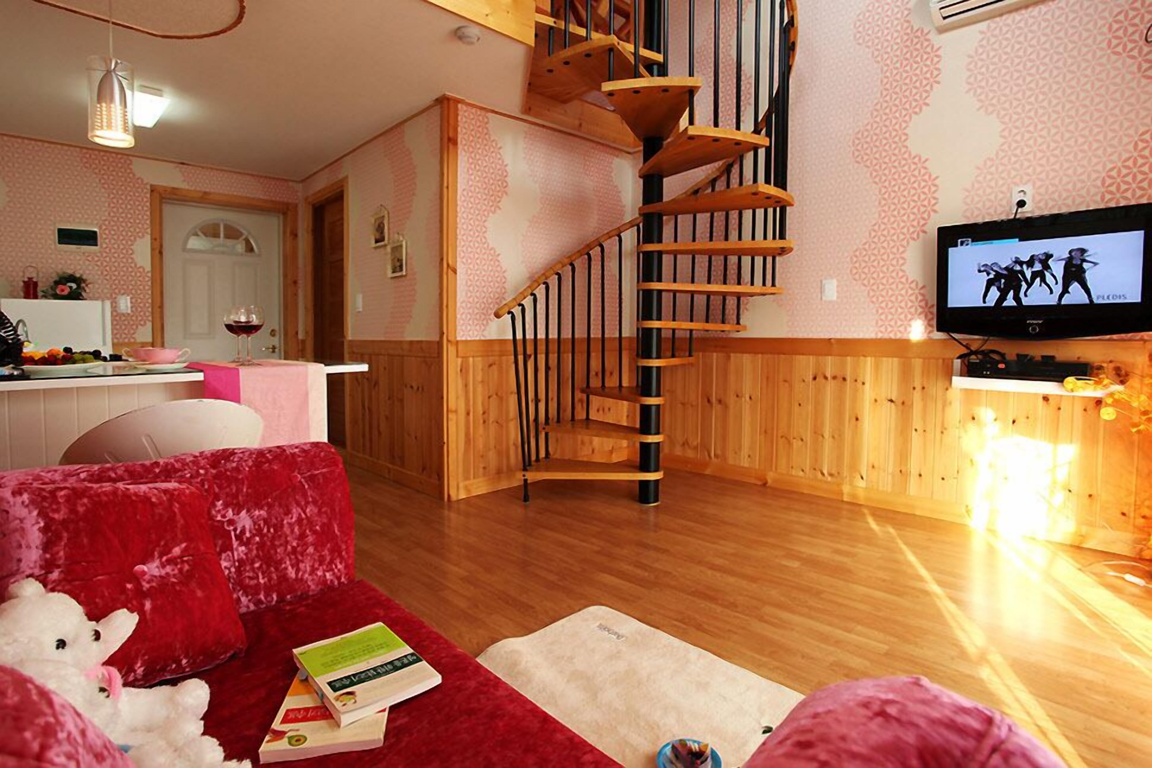 Una sala de estar acogedora con un sofá rojo, una escalera de madera, un televisor y una cocina al fondo.