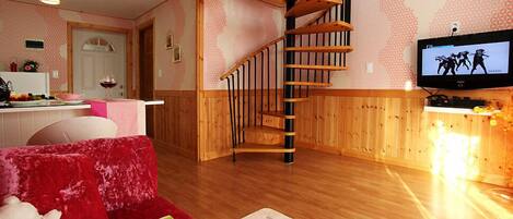 Una sala de estar acogedora con un sofá rojo, una escalera de madera, un televisor y una cocina al fondo.
